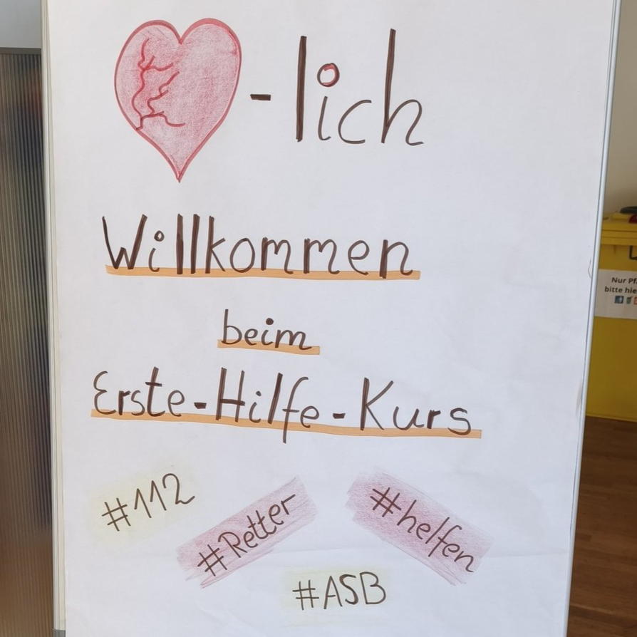 Herzlich willkommen zum Erste-Hilfe-Kurs Ein Flipchart steht neben einem Defibrillator. Auf dem Flipchart steht Willkommen zum Erste-Hilfe-Kurs.