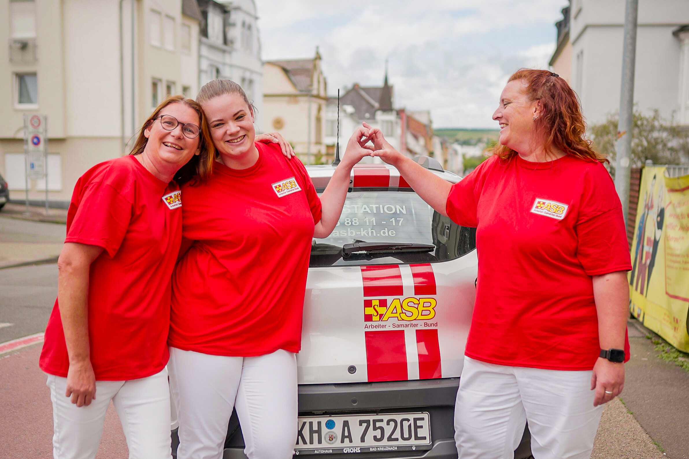 Mitarbeiterinnen am Dienstwagen Drei ASB-Mitarbeiterinnen auf der Straße neben einem ASB-Dienstwagen